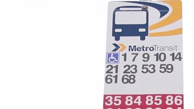 A current bus stop sign with many route numbers marked on it.