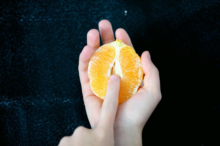 A finger pokes into a halved orange.